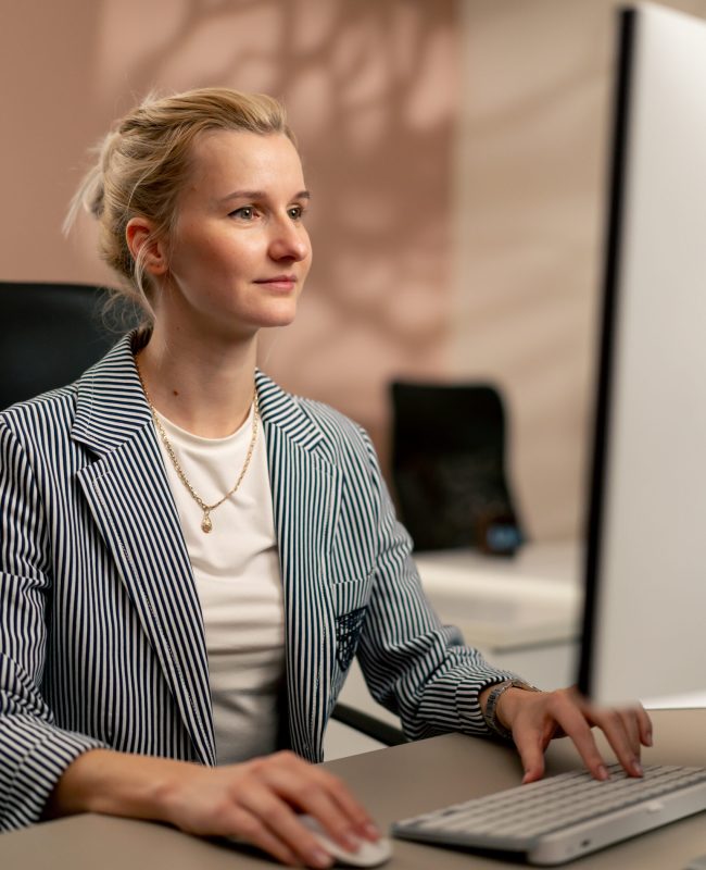 in a bright office with beige walls young blonde employee works at a white monitor on a light table modern office sun rays working on a project